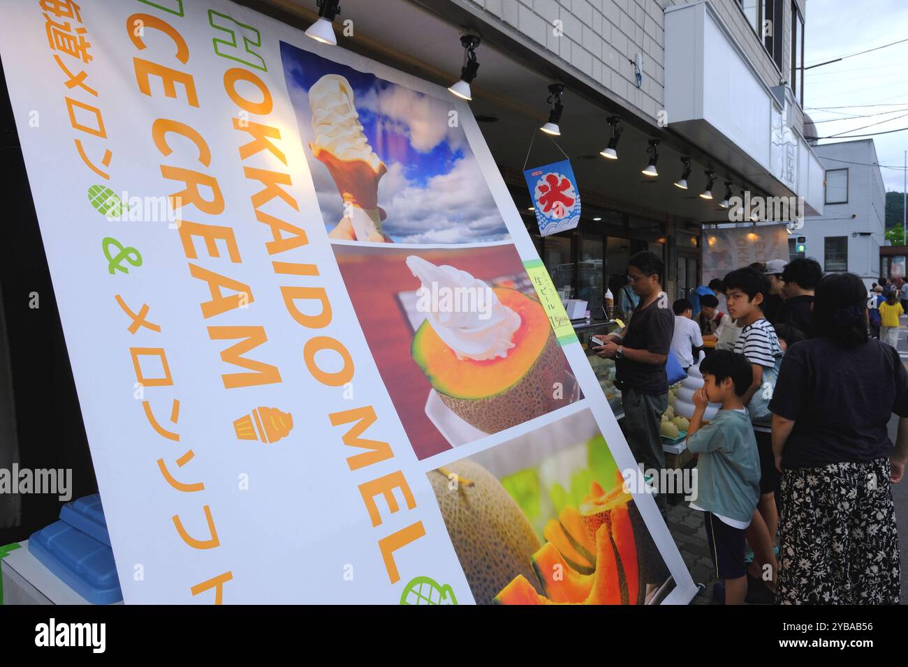 Customers waiting in line outside of a ice cream shop with an advertising banner of Hokkaido Melon ice cream beside.Otaru,Hokkaido.Japan Stock Photo