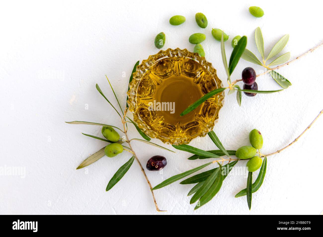 Olive oil in a crystal glass bowl, green and black olives in branches ...
