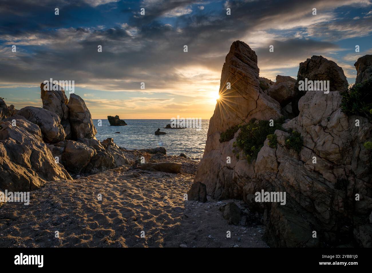 Sun Rays Behind Rocks A rocky beach with the sun setting over the sea casting highlights on ...