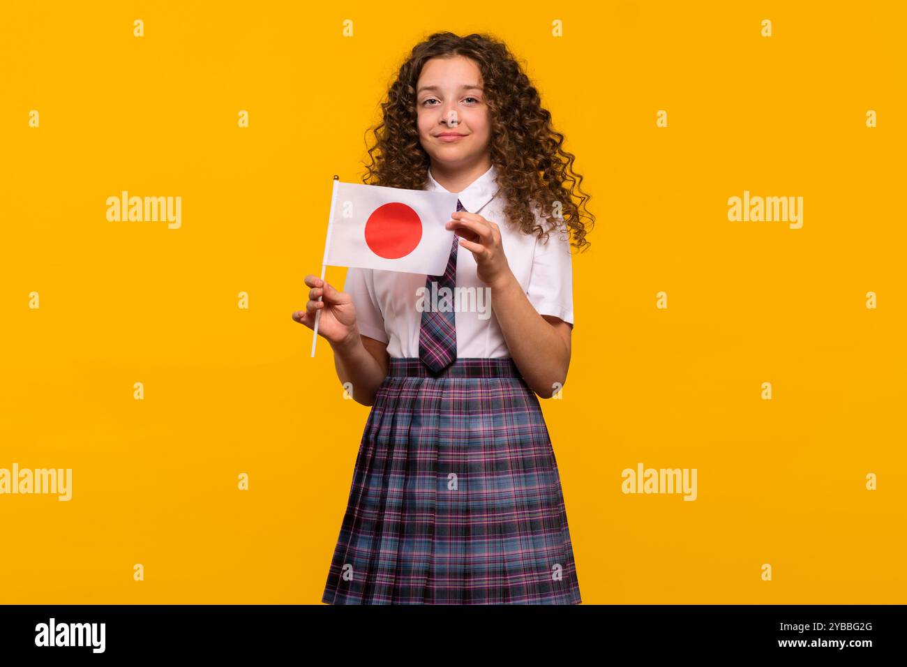 Girl holding Japanese flag in uniform, neutral expression. Foreign language learning concept. Stock Photo