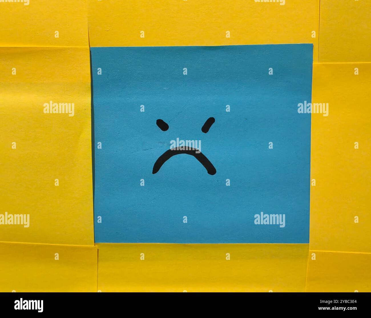 Emotional Contrast. Blue Face Sticky Note with Angry Expression Against a Yellow Background. Stock Photo
