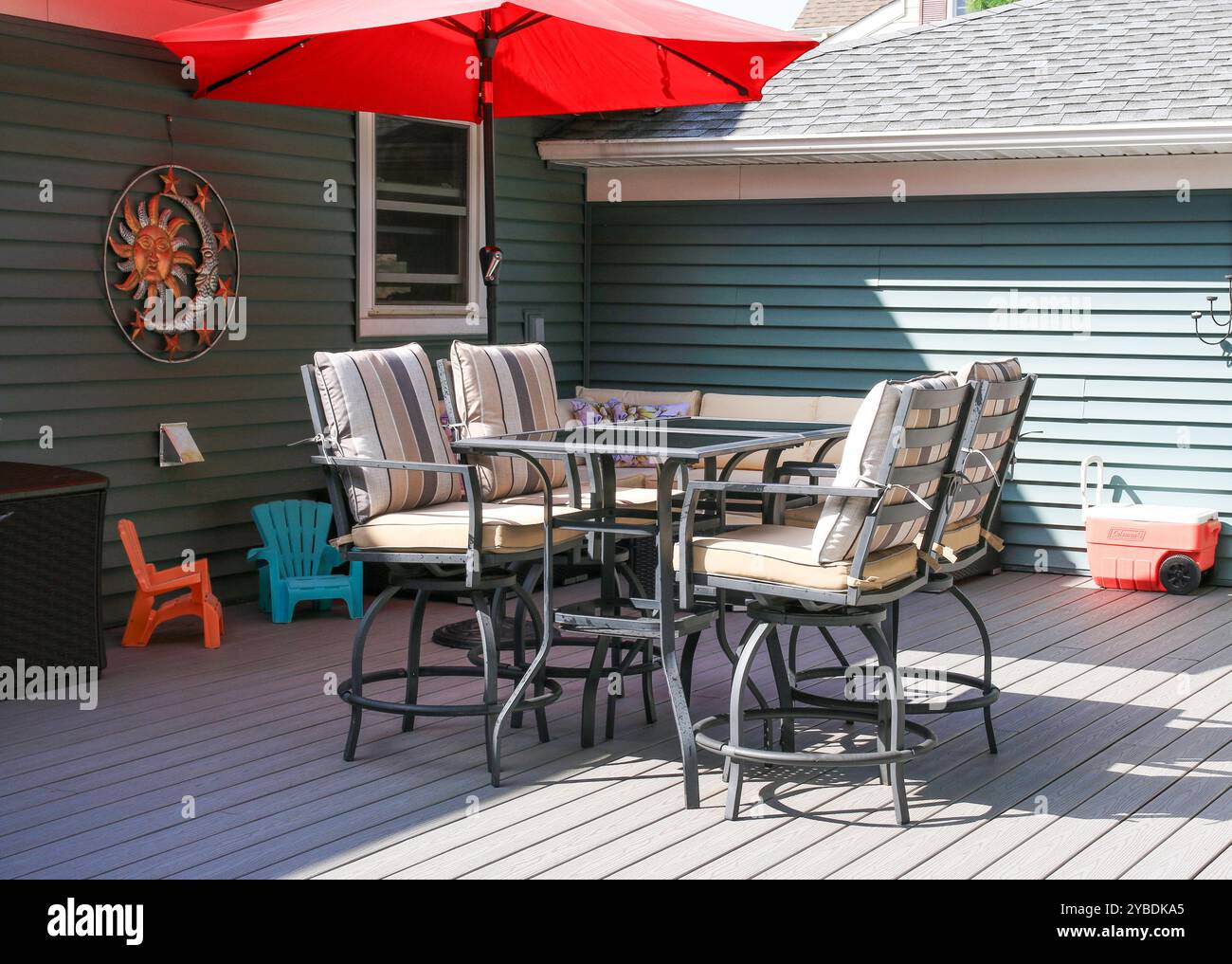 A spacious patio featuring bar stools, a round table, and a bright red umbrella for shade. Stock Photo