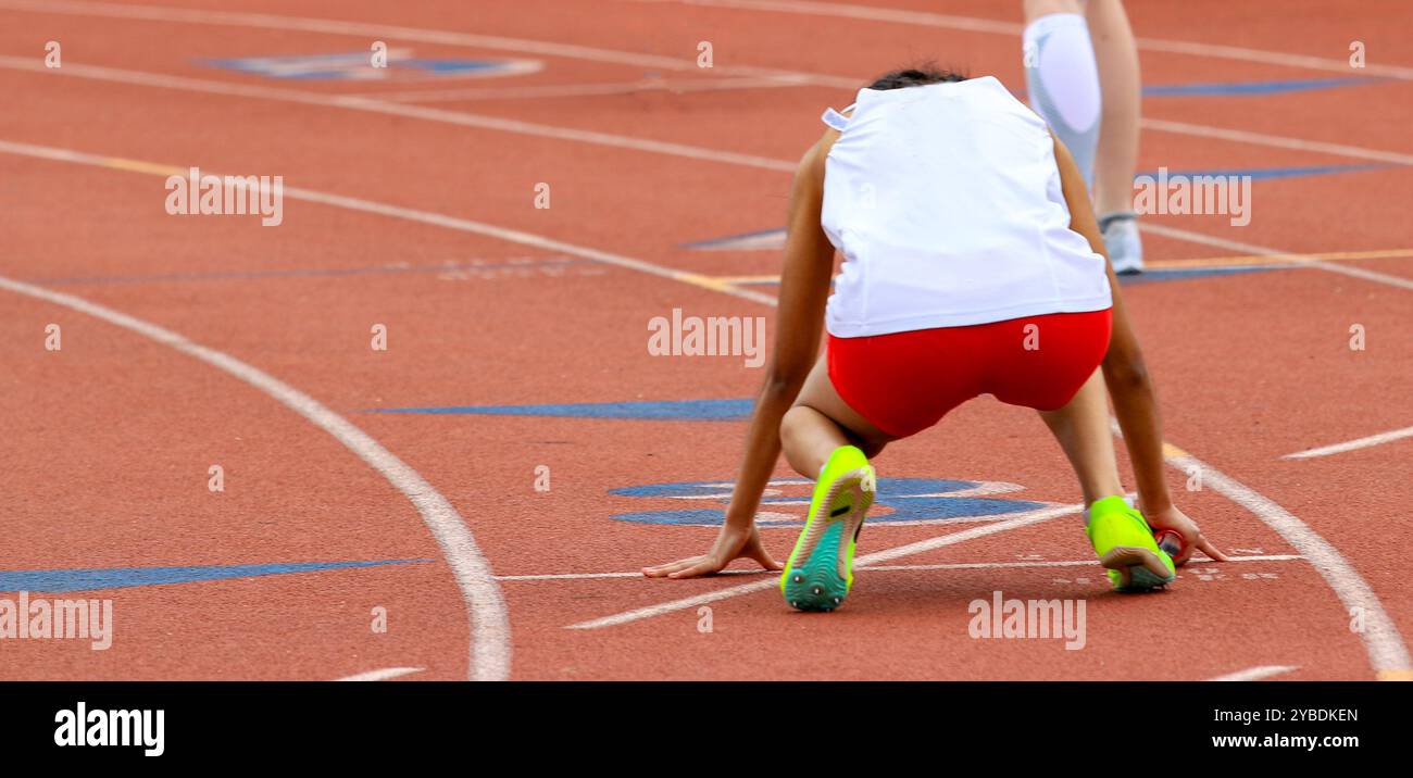 Rear view of a female high school runner ready to start a sprint relay ...