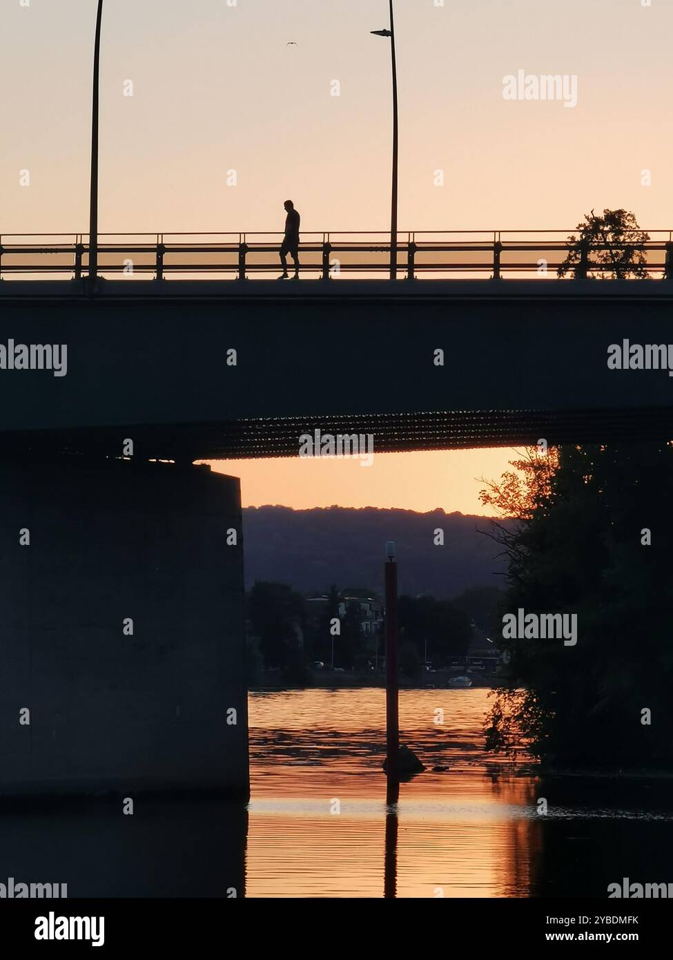 A solitary figure walks across Pont Clemenceau bridge during sunset over the serene River Seine in Vernon, Normandy, France - Smartphone Captured Stock Image A solitary figure walks across Pont Clemenceau bridge during sunset over the serene River Seine in Vernon, Normandy, France - Smartphone Captured Stock Image