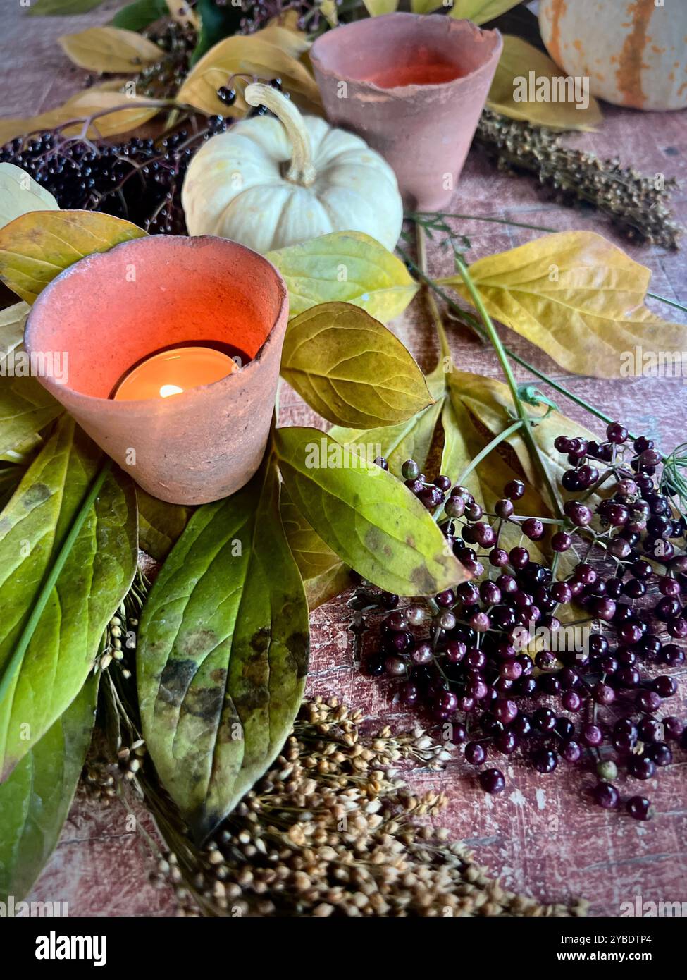 Cozy autumn arrangement with candles, small pumpkins, and berries, creating a warm and rustic centerpiece perfect for fall gatherings or Thanksgiving - Smartphone Captured Stock Image