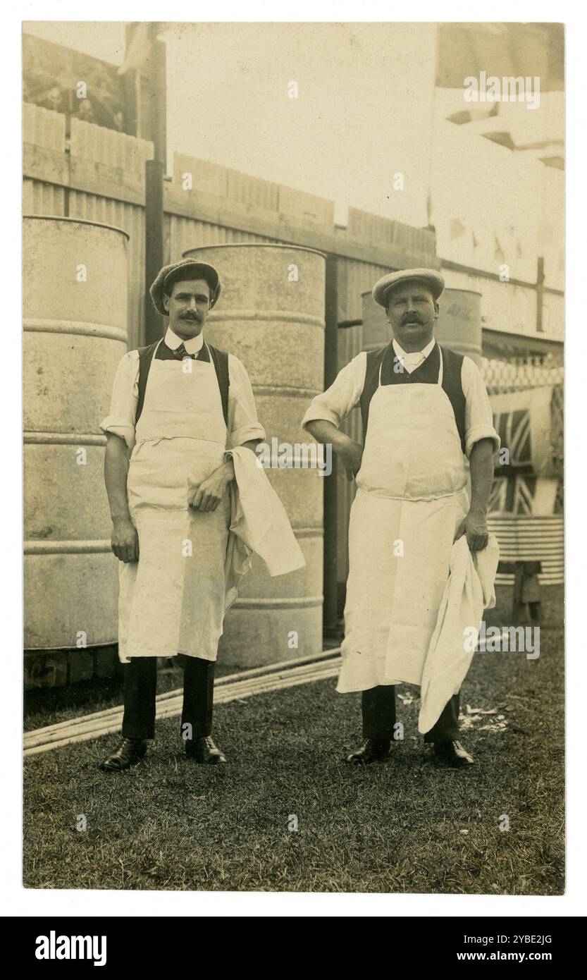 Early 1900's postcard of two working class men in aprons, possibly millers, next to large metal drums which were probably containers for corn and animal feed. Thought to be Talgarth Mill. The men are standing proudly to have their photograph taken, Maybe the new tenants of the mill. The drums are waiting to be installed. A new business venture. The patriotic Union Jack could indicate this was taken during WW1 period, circa 1914. By O. Jackson, Wellington Studio, Talgarth, Powys, Wales. Circa 1910 Stock Photo
