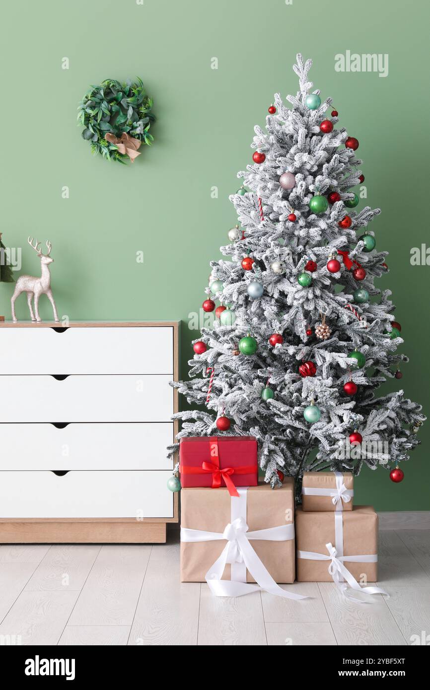 Decorated Christmas tree with gifts and dresser against green wall ...