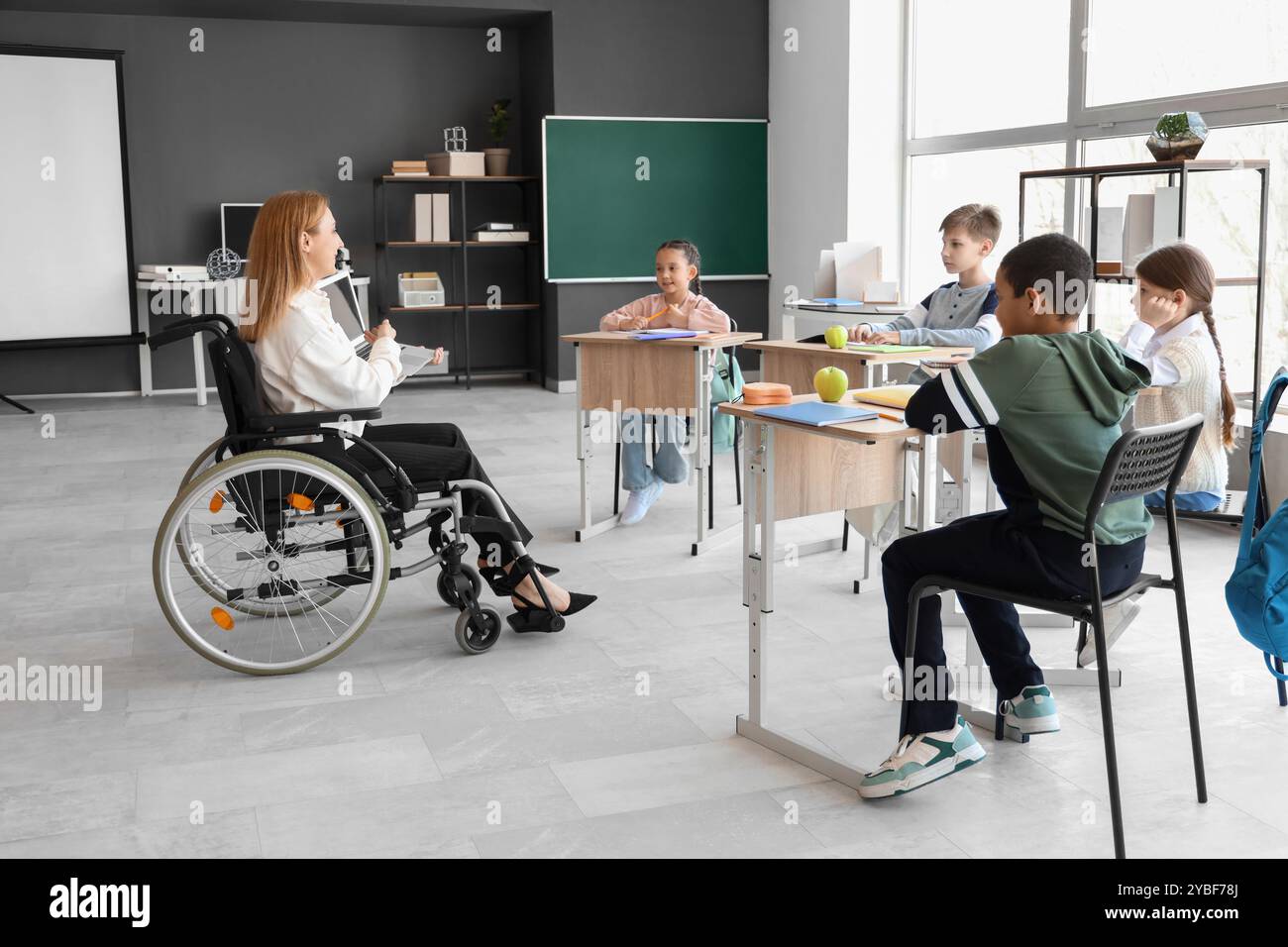 Mature teacher in wheelchair with laptop conducting lesson at school ...