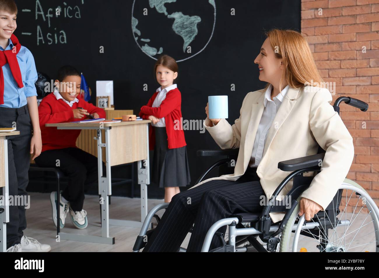 Mature Geography teacher in wheelchair with coffee and little pupils at ...