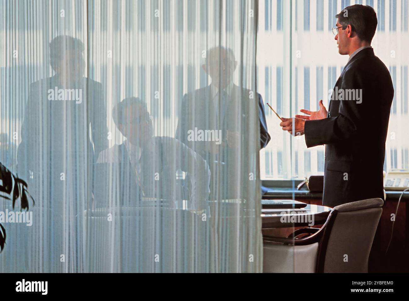 A presenter discusses important topics with colleagues in an office, with silhouettes of participants visible through a sheer curtain. Stock Photo