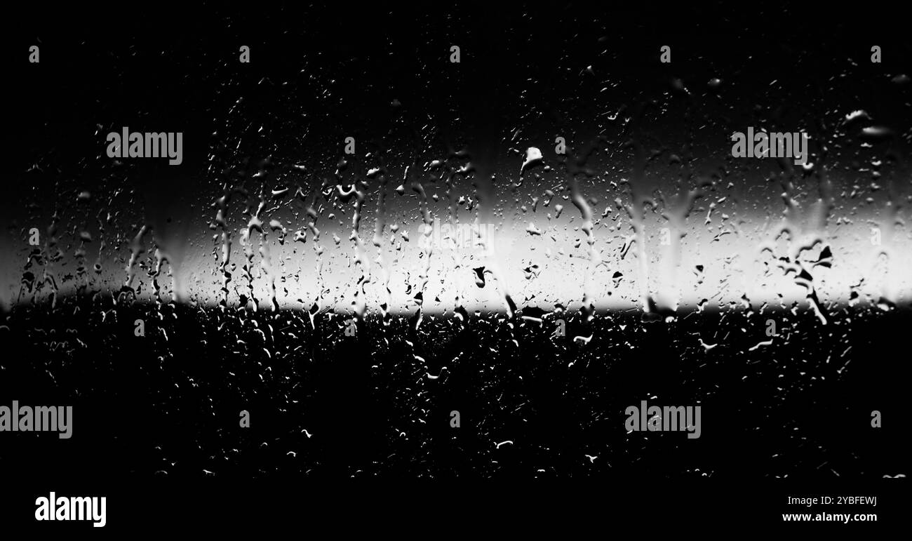 Raindrops on a window during a stormy evening, creating a moody atmosphere with blurred silhouettes outdoors Stock Photo