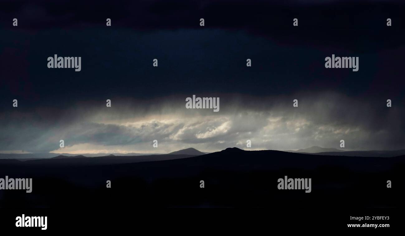 Clouds gather ominously over Sangre de Cristo mountains in New Mexico as twilight approaches, casting a moody atmosphere across the desert landscape Stock Photo