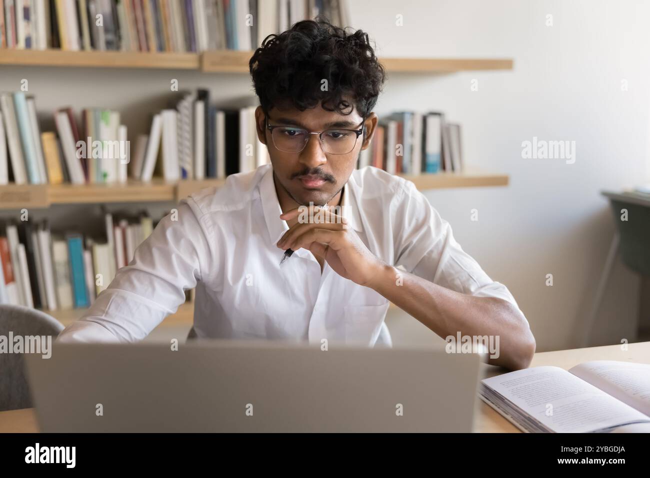Focused handsome Indian student man studying online at laptop Stock Photo