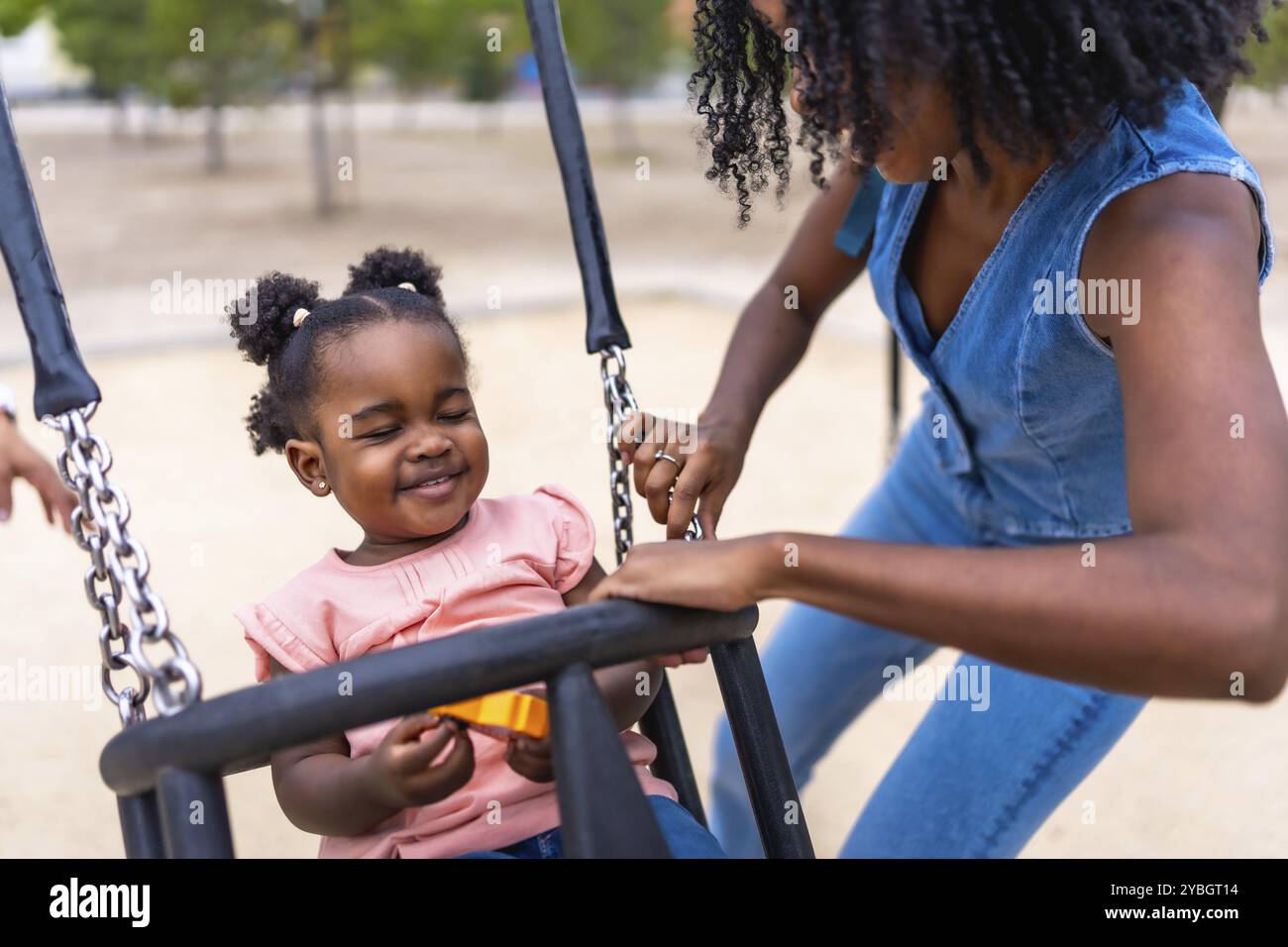 African mother and baby girl having fun swinging in a public park Stock Photo