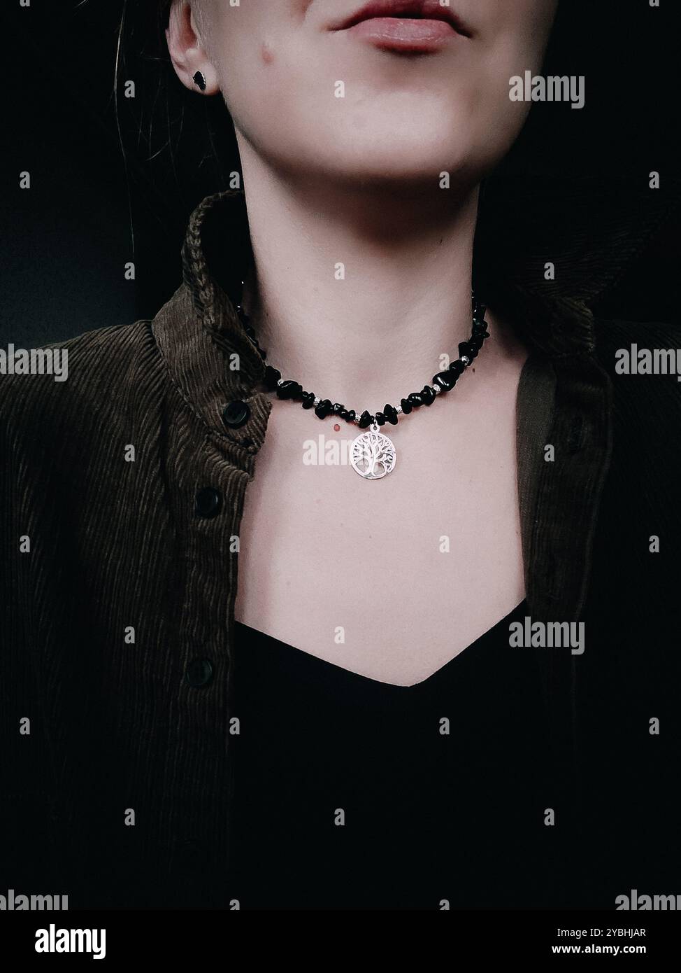 Black obsidian choker with tree of life pendant on woman's neck Natural stone chunky necklace with tree of life charm Woman without face close up - Smartphone Captured Stock Image
