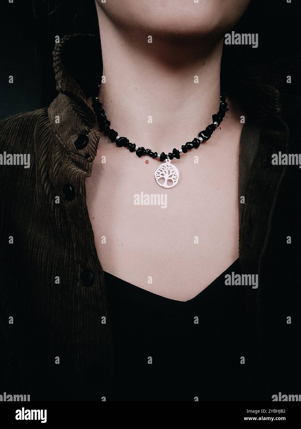Black obsidian choker with tree of life pendant on woman's neck Natural stone chunky necklace with tree of life charm Woman without face close up - Smartphone Captured Stock Image