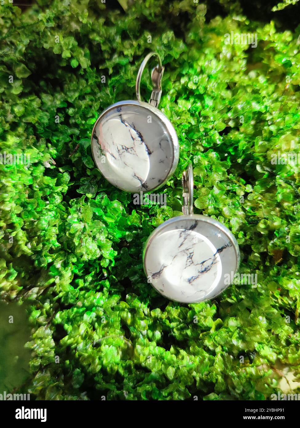 Handmade resin round marble texture stone earrings transparent finish at green moss background close. Leverback hooks, nature-inspired jewelry - Smartphone Captured Stock Image