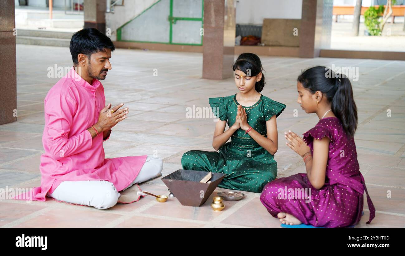 An Indian family in traditional attire performs a Yagya or Havan, led by a priest, to balance energies in their home. This sacred pooja is for harmony Stock Photo