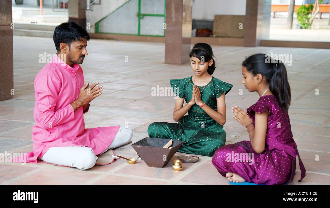 An Indian family in traditional attire performs a Yagya or Havan, led by a priest, to balance energies in their home. This sacred pooja is for harmony Stock Photo