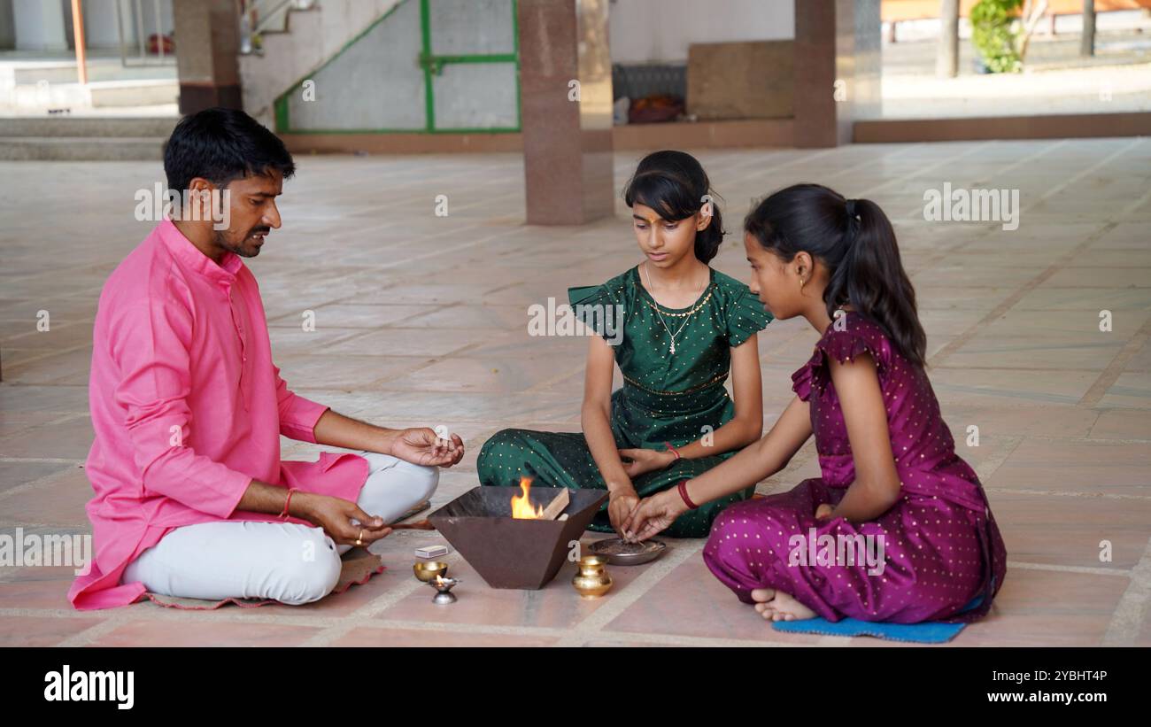An Indian family in traditional attire performs a Yagya or Havan, led by a priest, to balance energies in their home. This sacred pooja is for harmony Stock Photo