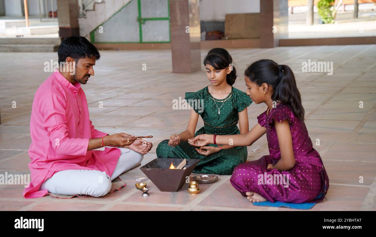 An Indian family in traditional attire performs a Yagya or Havan, led by a priest, to balance energies in their home. This sacred pooja is for harmony Stock Photo