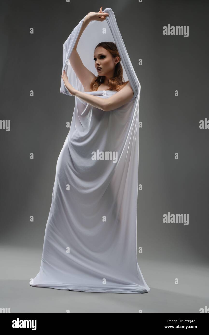 Model elegantly poses with flowing white fabric in a studio setting Stock Photo