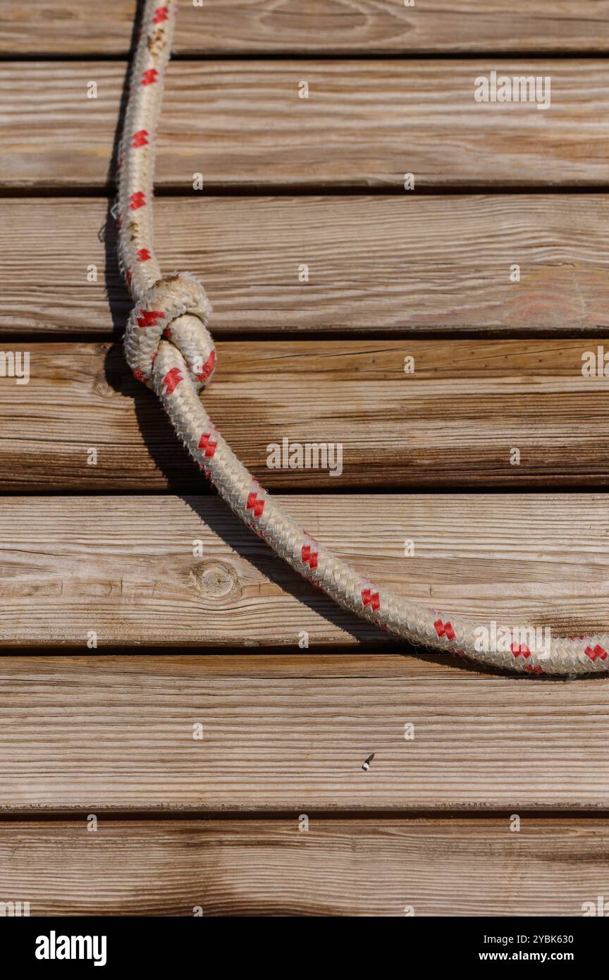 Tightly coiled, the rope, featuring distinct red markings, rests on rustic wooden planks, reflecting the warm sunlight of a peaceful afternoon, creati Stock Photo