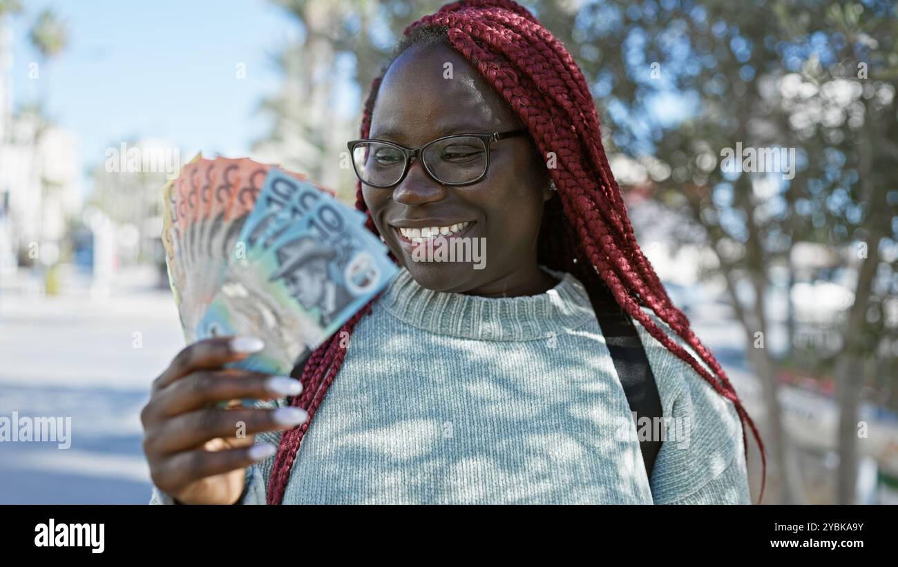 A smiling african woman with braids holding australian dollars outdoors ...