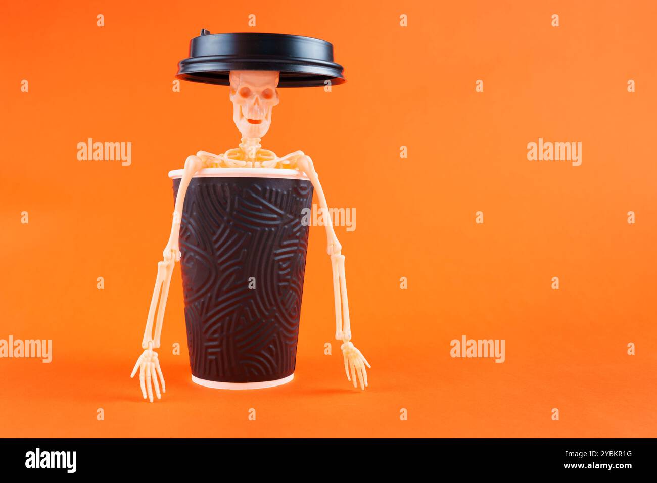 Skeleton figure inside a coffee cup with a lid, set against an orange background. Represents Halloween themes or coffee shop promotions. Stock Photo