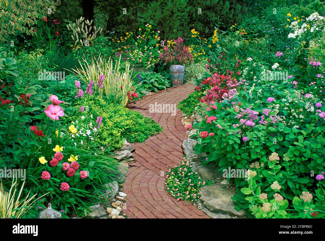 Scalloping brick pathway through blooming garden and painted Mexican vase, Missouri USA Stock Photo