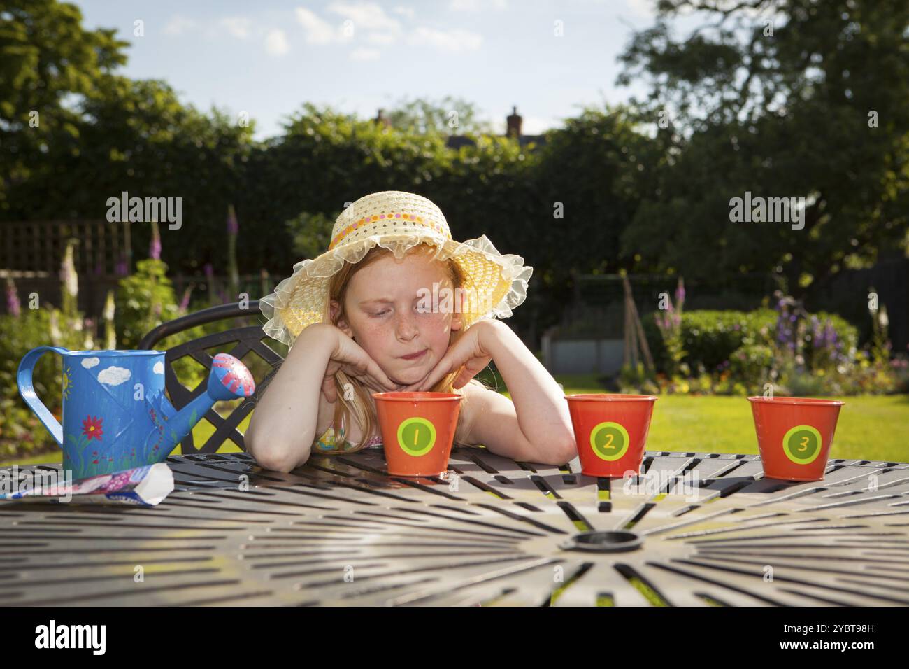 Pre teen caucasian girl watering flower pots in a garden themes of waiting impatience gardener care Stock Photo