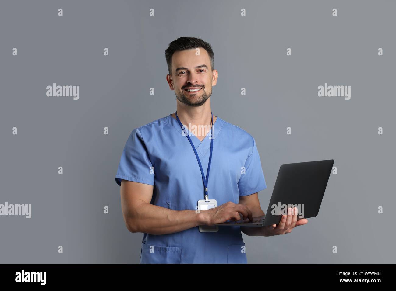 Smiling nurse with badge and laptop on grey background Stock Photo - Alamy