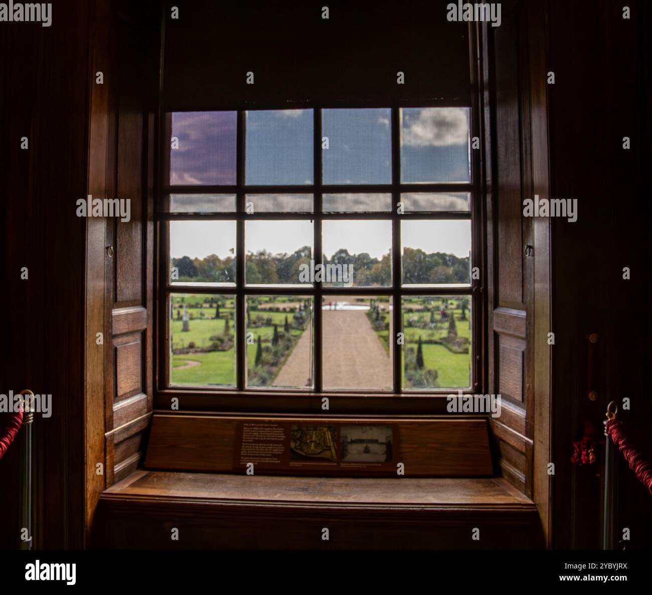 View through a wooden window with open shutters overlooking a beautifully manicured garden and pathway Hampton Court Palace Stock Photo