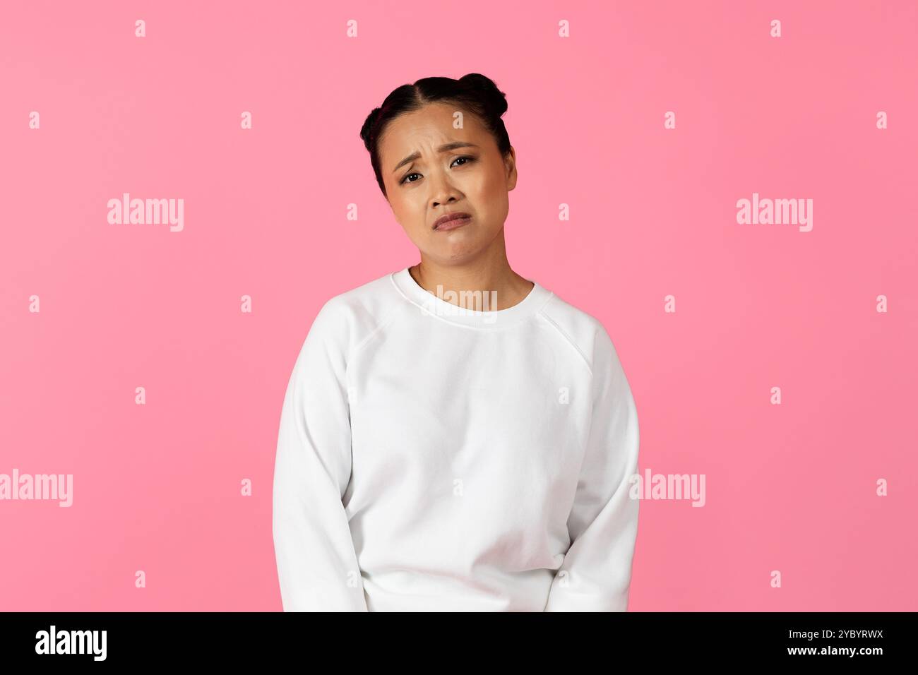 Young woman expressing concern against a vibrant pink background in casual wear Stock Photo