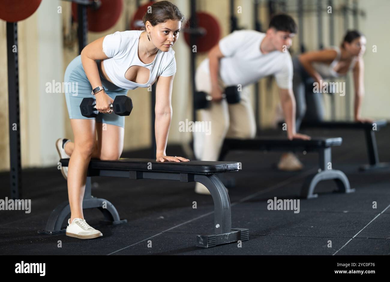 Athletic young woman pumping her biceps with a dumbbell while leaning ...