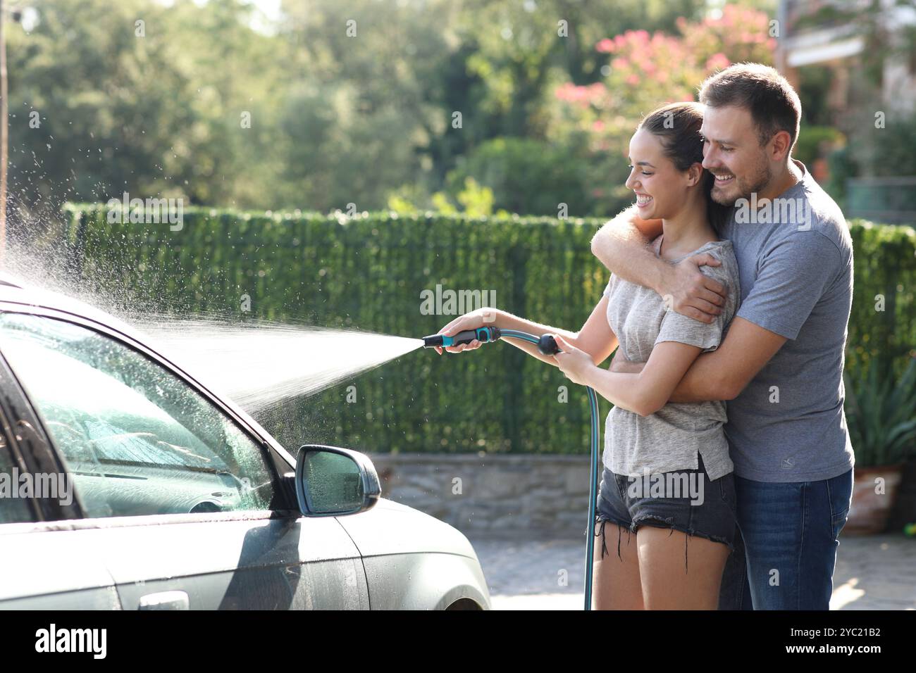 Happy couple washing car in the garden using hosepipe Stock Photo