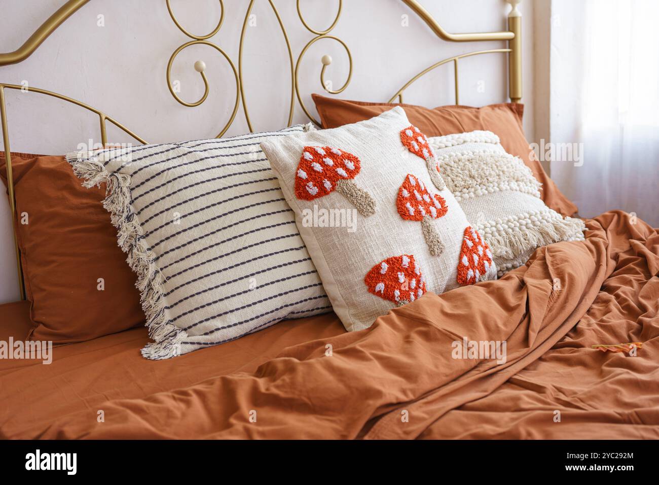 Beautifully styled bed features warm, rich toned bedding and charming decorative pillows with mushroom patterns against of metal forged headboard back Stock Photo