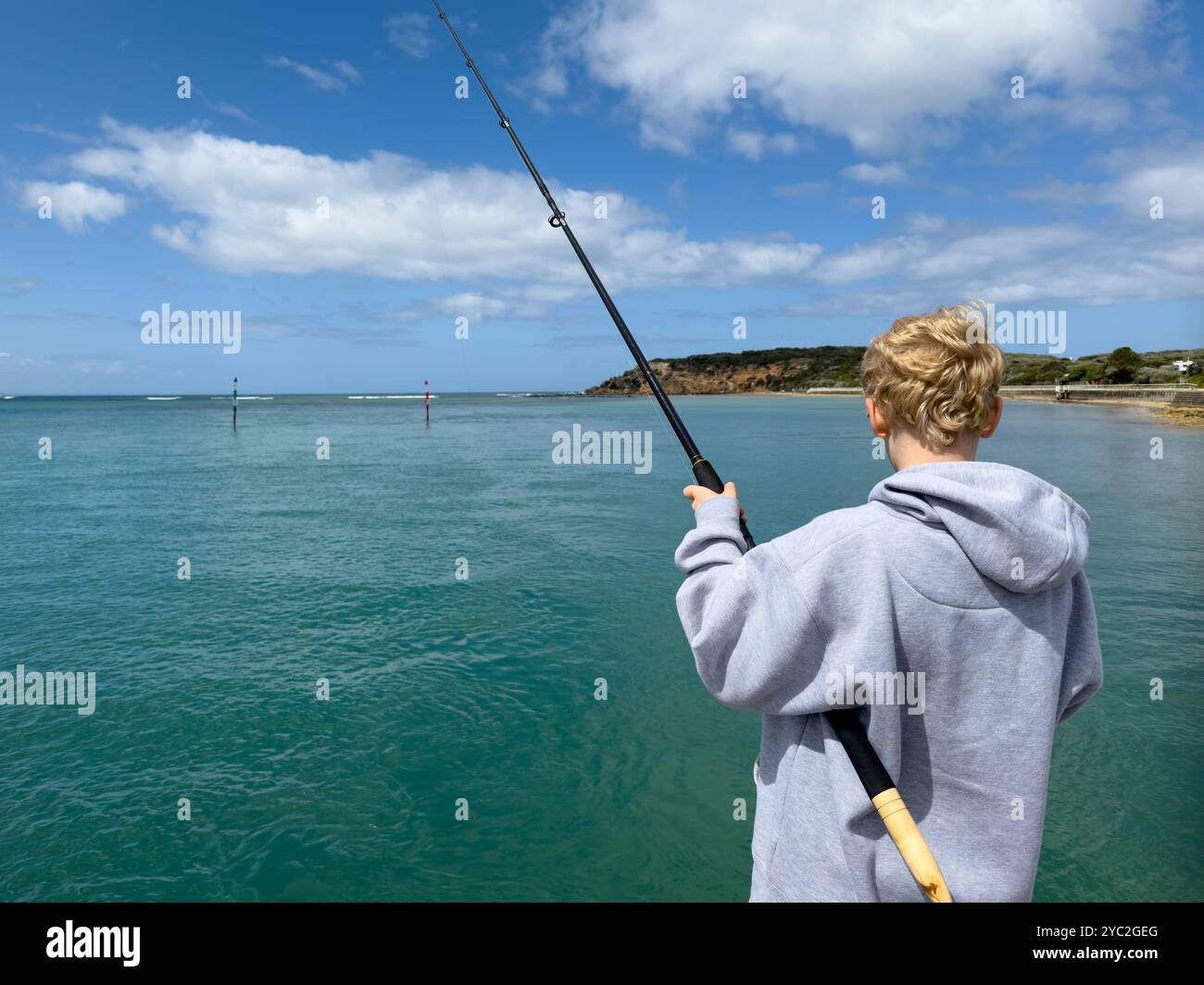 Boy casting a fishing line, looking out at blue waters Barwon Heads Stock Photo