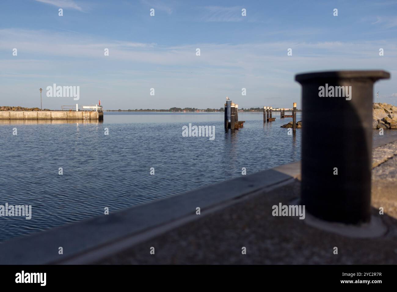 A peaceful coastal harbor scene with calm waters and a clear blue sky, captured near a stone pier and mooring bollard, creating a tranquil maritime at Stock Photo