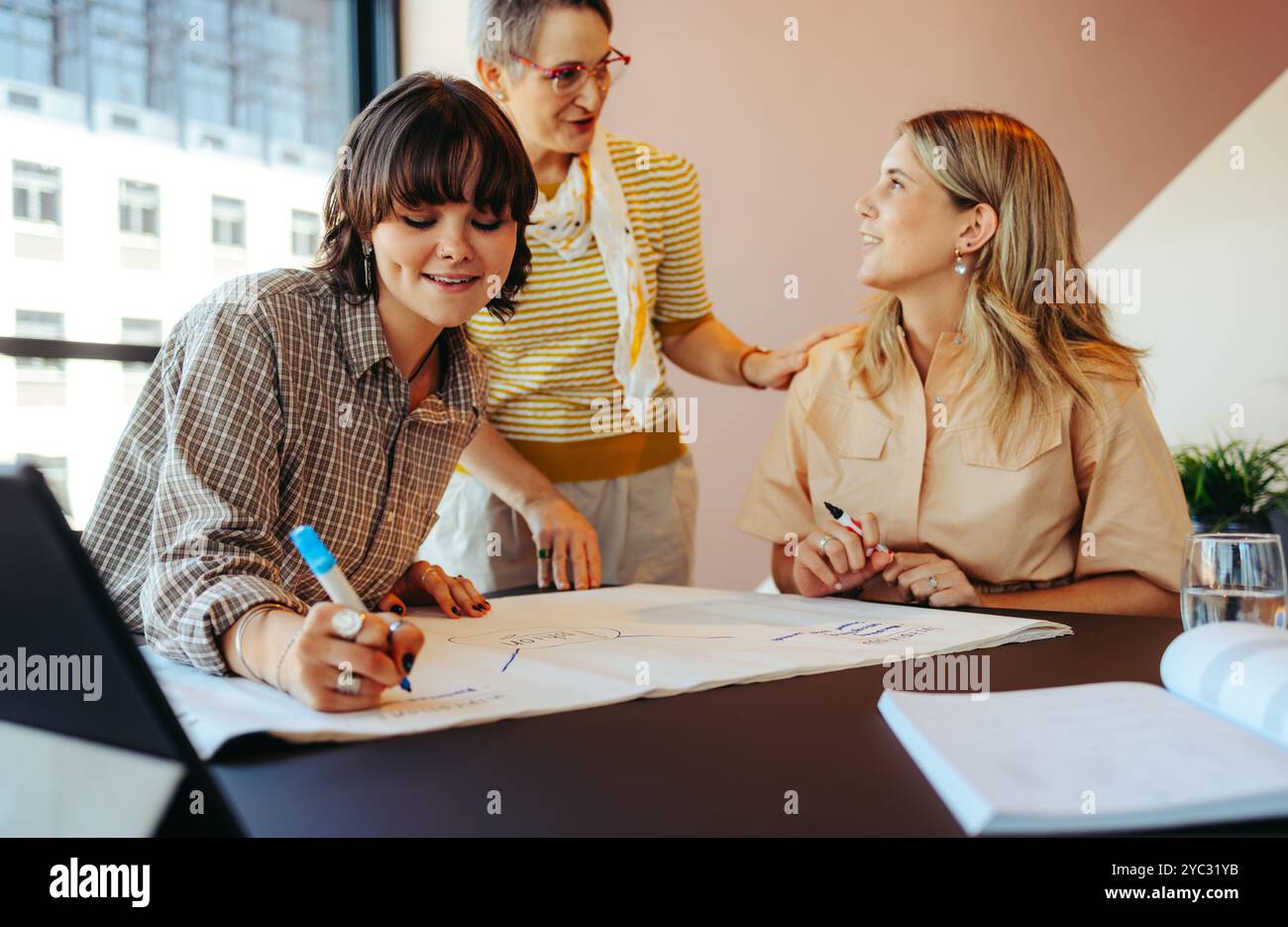A mentor guides and assists students as they work together on a creative project in a bright city office. Collaborative learning and support. Stock Photo