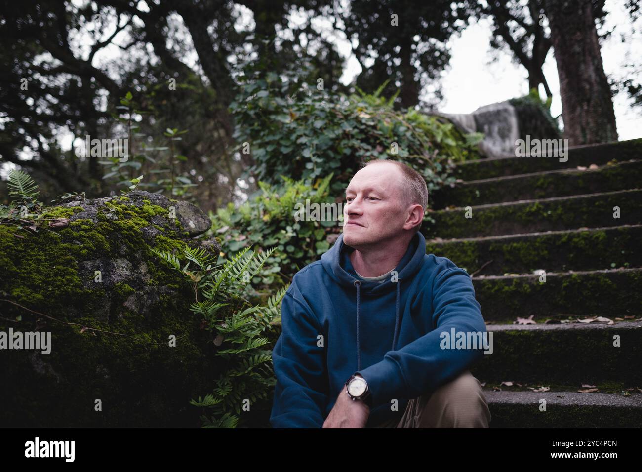 A man sitting on the stone steps in the park during autumn, taking in the cool breeze and the peacefulness of the season. Stock Photo