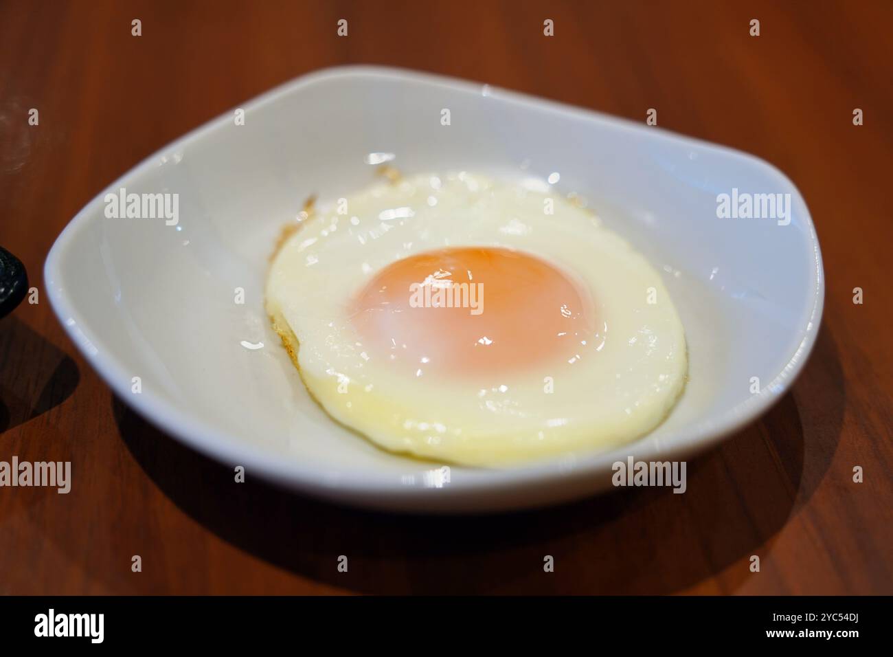 Fried egg in white bowl on wooden table Stock Photo