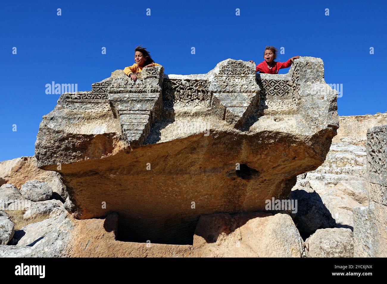 Sanliurfa, Turkey. 19th Oct, 2024. Two girls play on the inscriptions of the monument in the backyard of the Assyrian temple. In the village of Buyuk Senem, about 70 kilometres from the city of Sanliurfa in southeastern Turkey, the ancient Senem caves in the same area as the magnificent 3-storey Syriac temple dating from the 5th century A.D. are used by villagers as houses and animal shelters. Credit: SOPA Images Limited/Alamy Live News Stock Photo