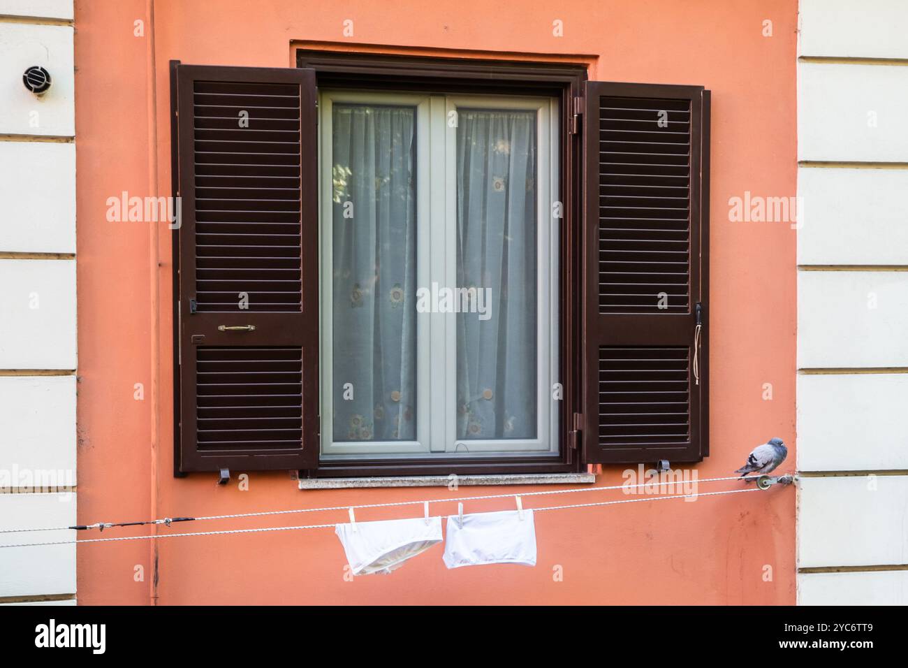 Window with open wooden shutters and laundry stretched outside on the ...