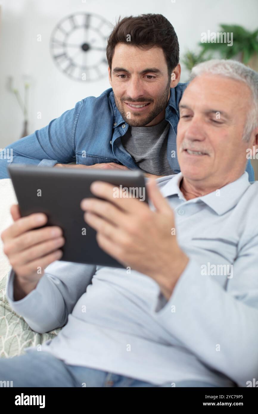 son teaching retiree dad to use banking app on tablet Stock Photo