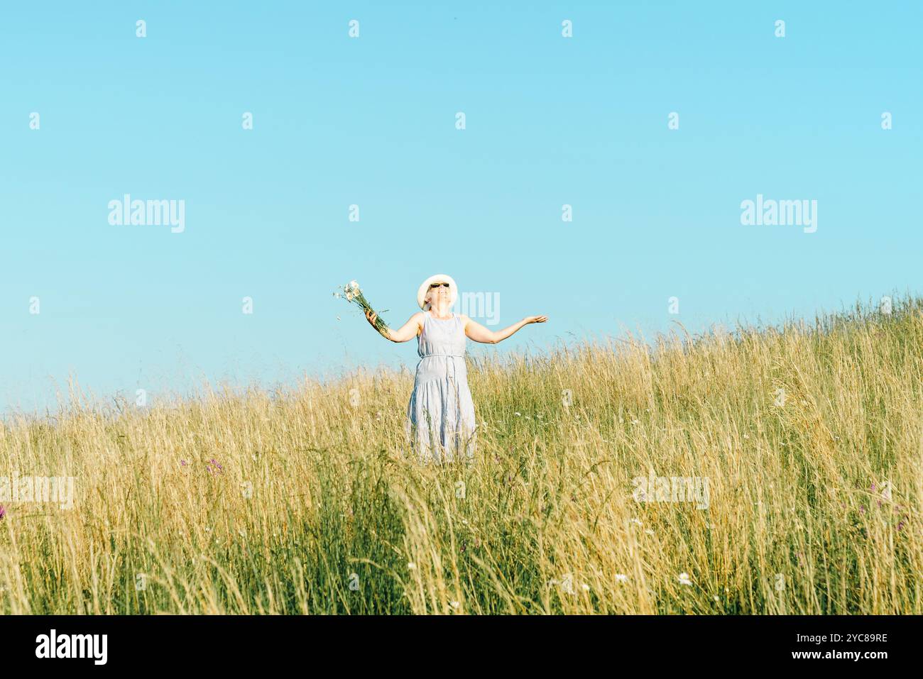 Happy mature woman with wildflowers in a tall grass field on a bright summer day. Stock Photo