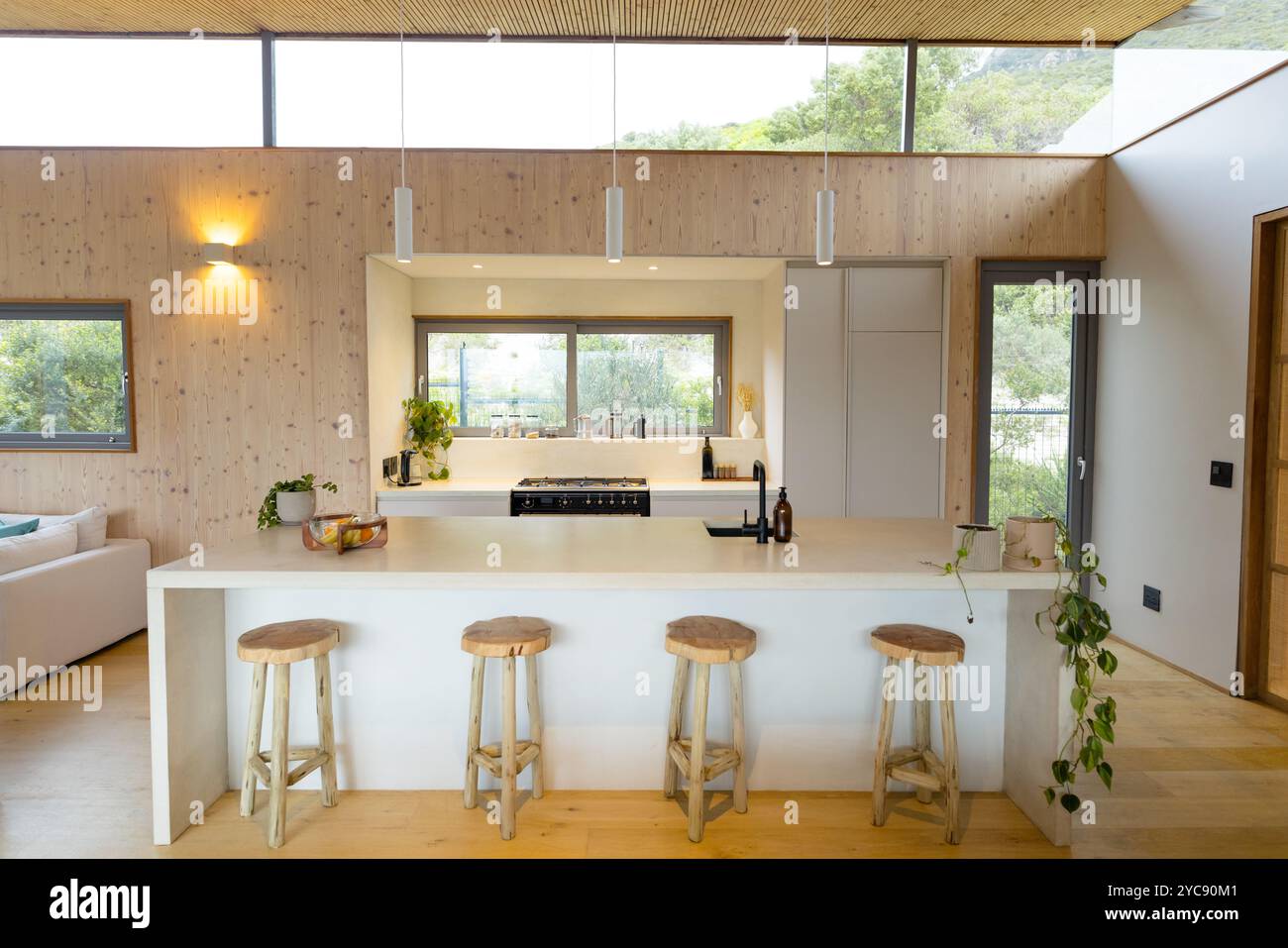 Modern kitchen with wooden stools and large windows, inviting natural ...