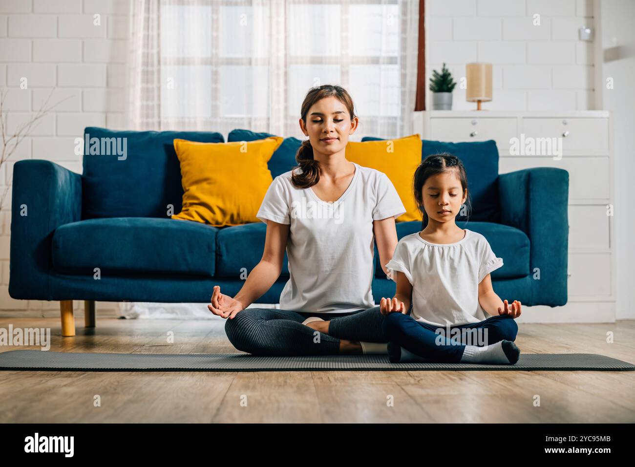 A mother and her daughter find serenity in family yoga sitting in lotus ...