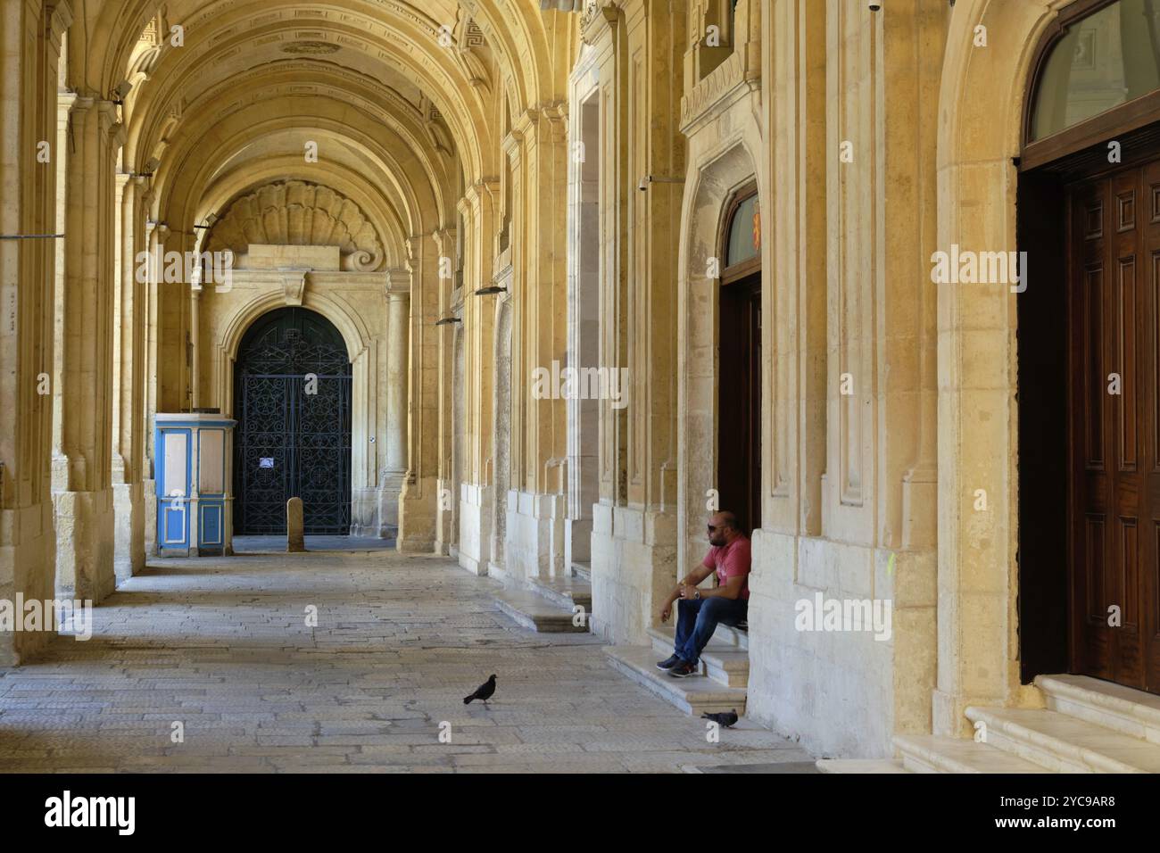 A man with his sandwich and two hungry pigeons in the archway of the National Library, Valletta, Malta, Europe Stock Photo