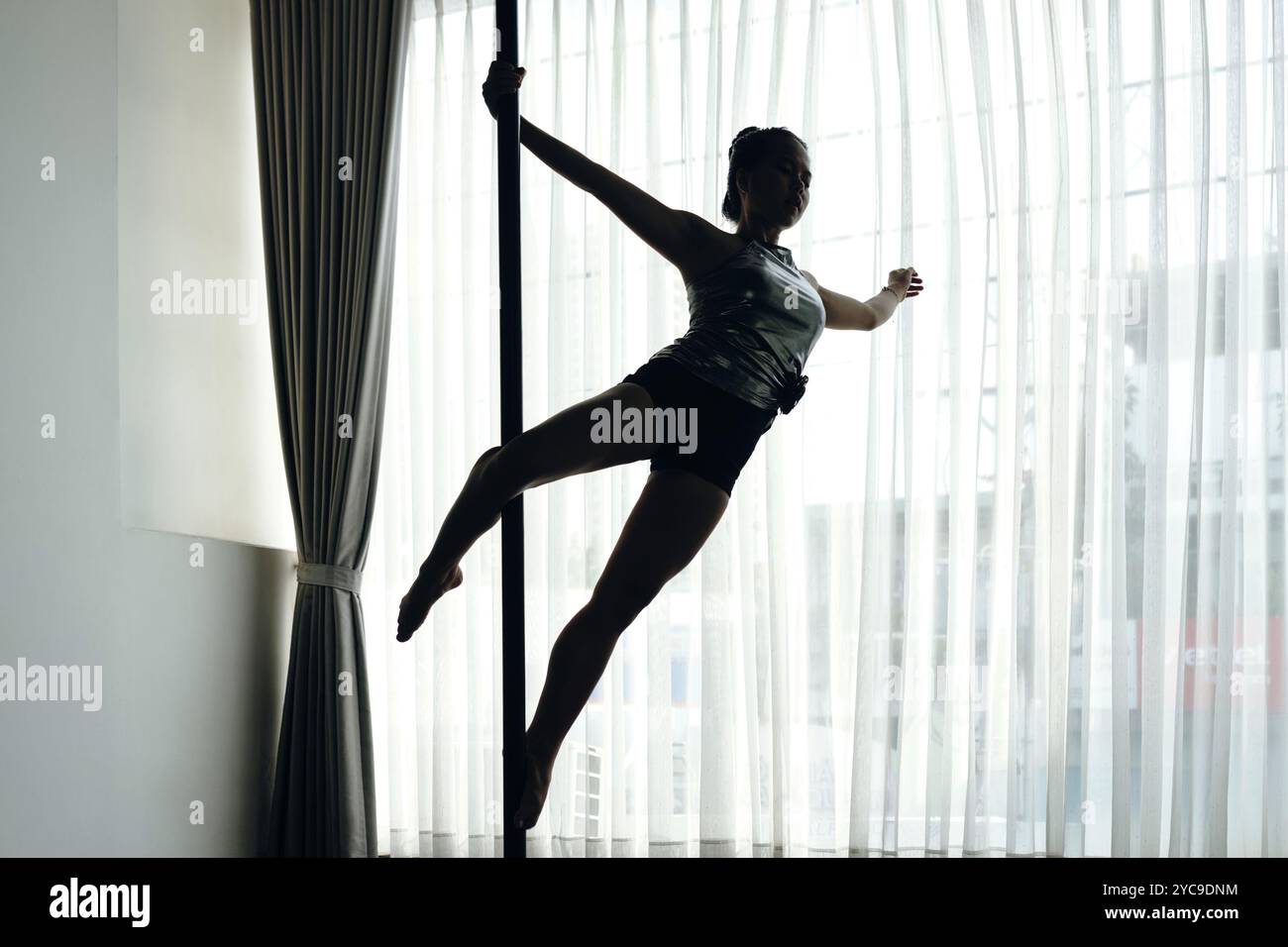 Practicing Silhouette Pole Dance Against Window Light Stock Photo